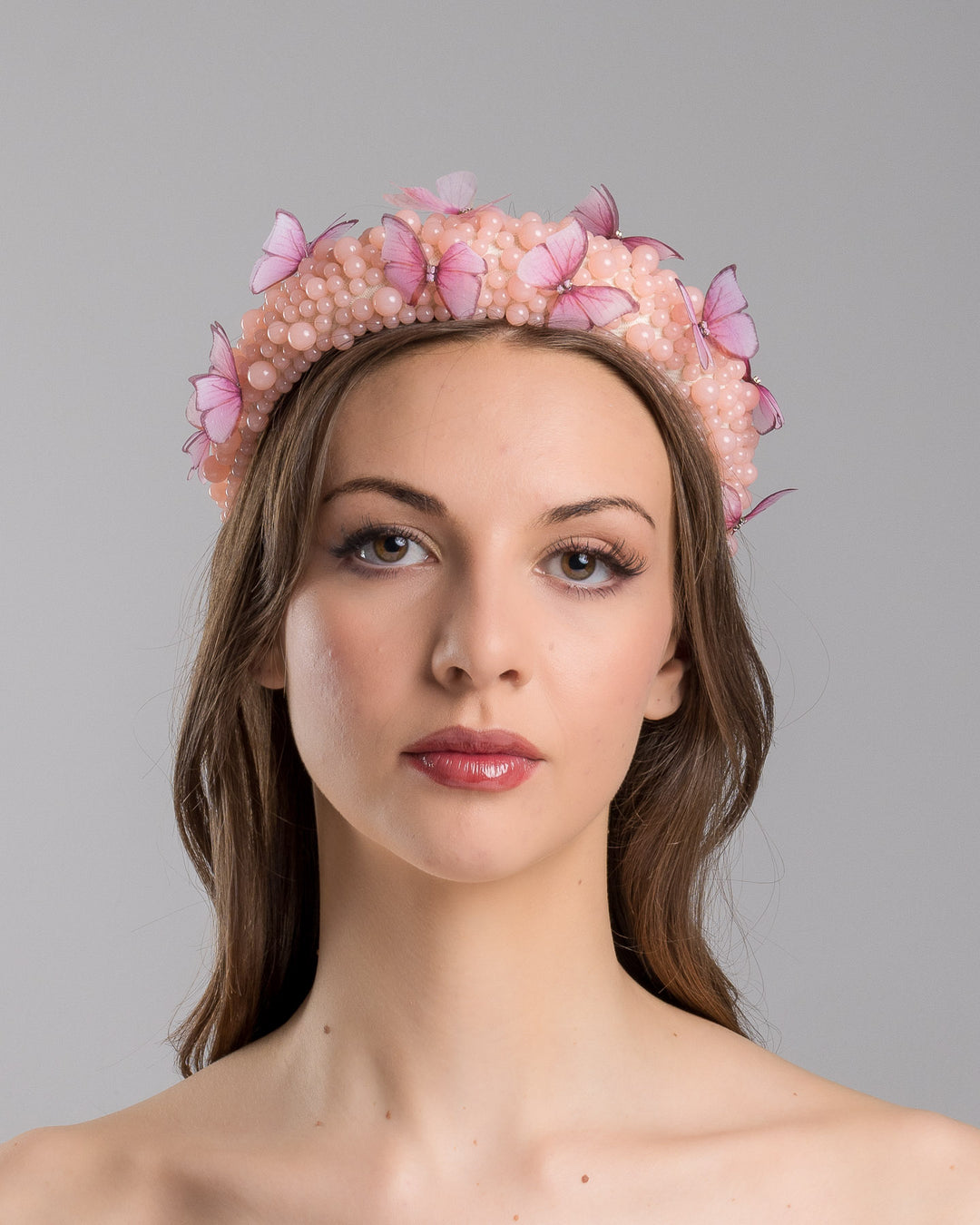 Model is showcasing the front side close up of high headband decorated with different sized mat peach beads and scattered pink organza butterflies with crystal centres. Made by Merve Bayindir millinery.