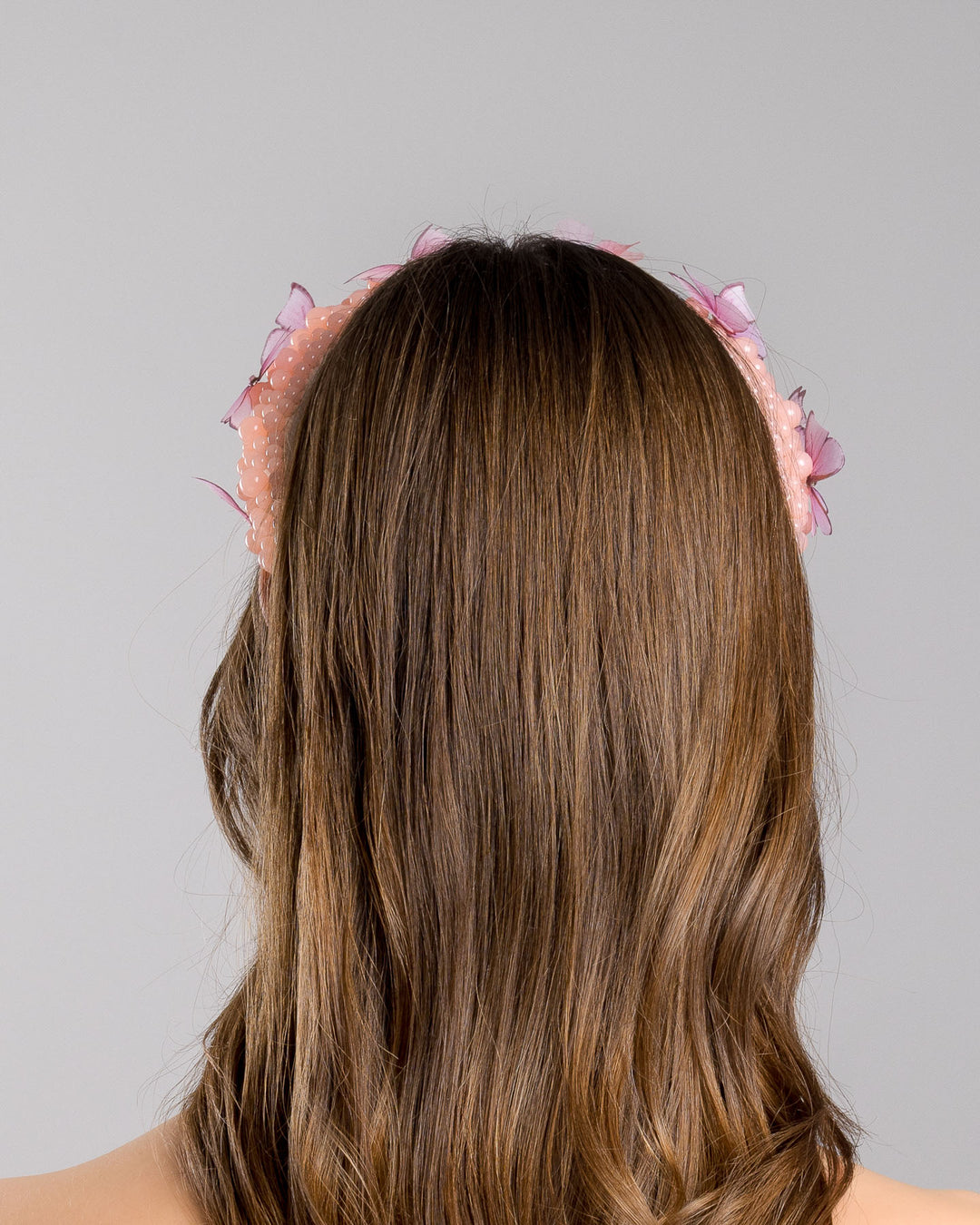 Model is showcasing the backside close up of high headband decorated with different sized mat peach beads and scattered pink organza butterflies with crystal centres. Made by Merve Bayindir millinery.