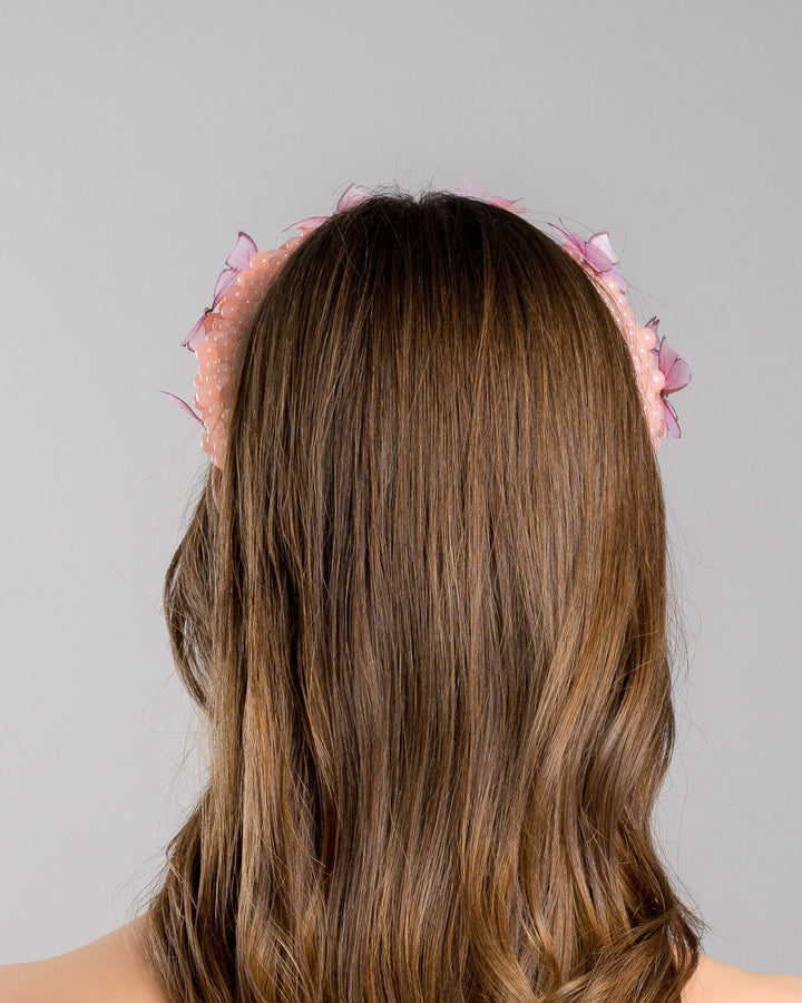 Model is showcasing the backside close up of high headband decorated with different sized mat peach beads and scattered pink organza butterflies with crystal centres. Made by Merve Bayindir millinery.