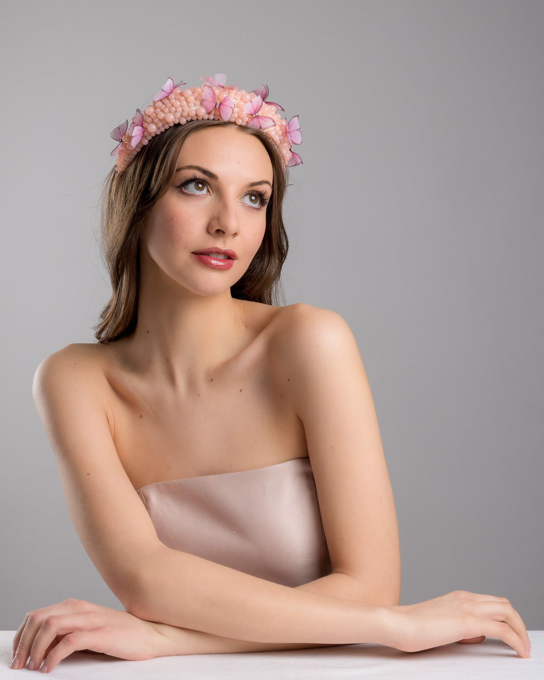 Female model posing wearing Cherry high headband decorated with different sized mat peach beads and scattered pink organza butterflies with crystal centres. Made by Merve Bayindir millinery.