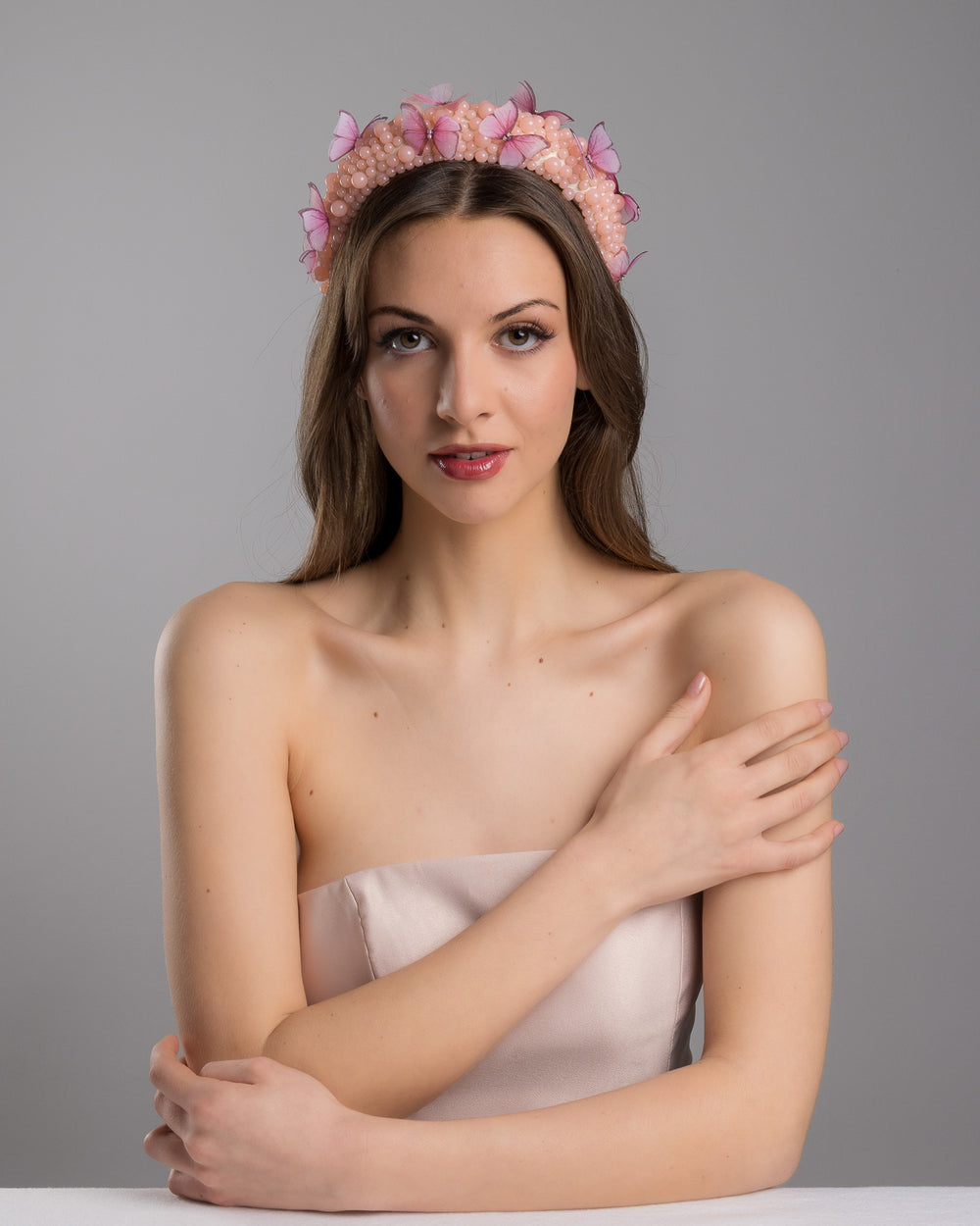 Female model posing wearing Cherry high headband decorated with different sized mat peach beads and scattered pink organza butterflies with crystal centres. Made by Merve Bayindir millinery.