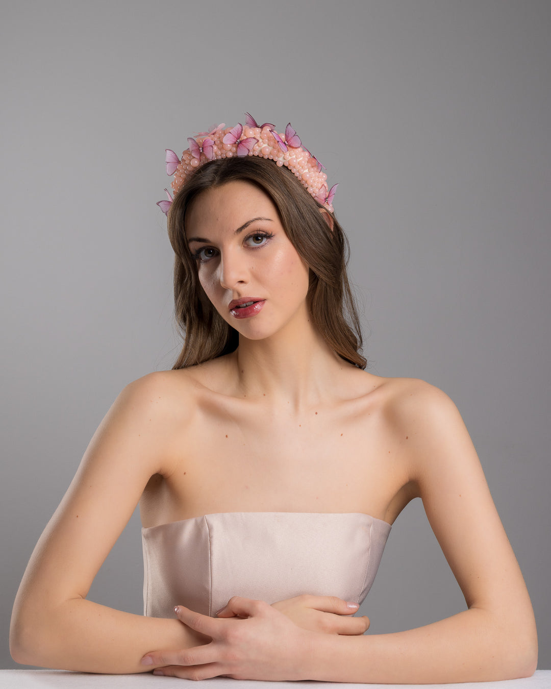 Female model posing wearing Cherry high headband decorated with different sized mat peach beads and scattered pink organza butterflies with crystal centres. Made by Merve Bayindir millinery.