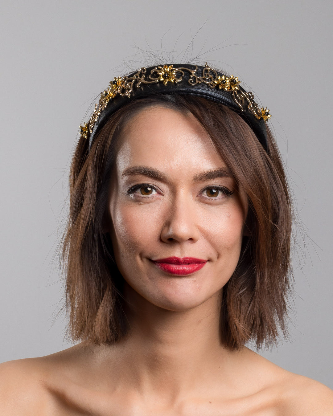 The model is showcasing the front side close up of the wide black satin headband embellished with ornate gold filigree scrollwork and small metallic floral accents, creating a regal, baroque-inspired statement design.
Designed and made by Merve Bayindir Millinery.
