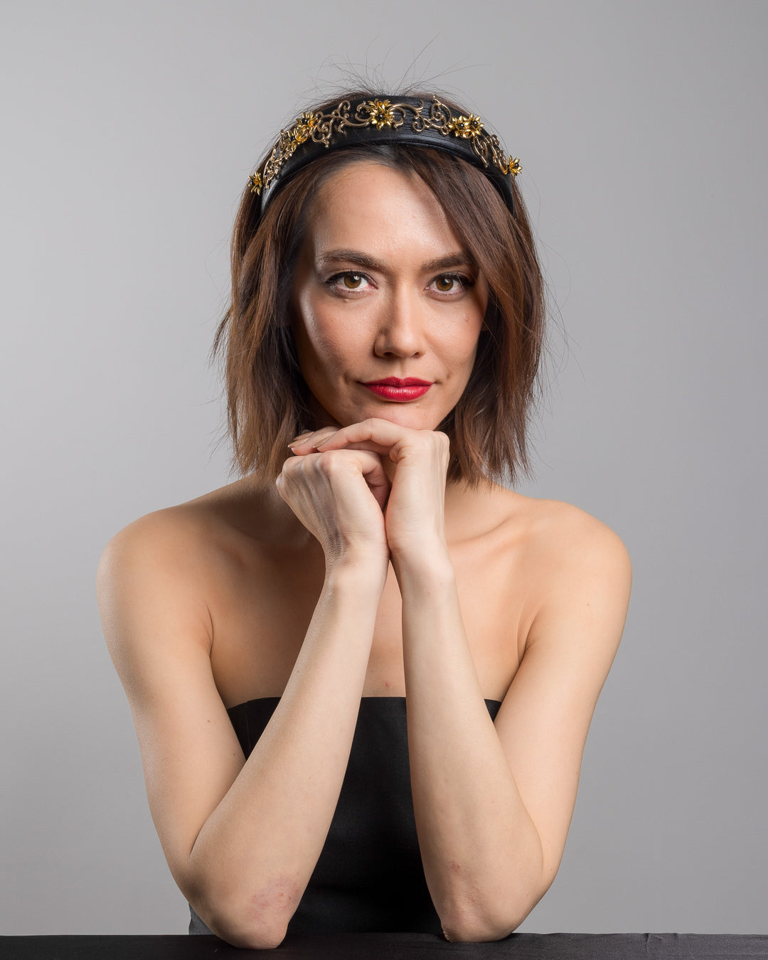 The female model is posing, wearing Doreal, the wide black satin headband embellished with ornate gold filigree scrollwork and small metallic floral accents, creating a regal, baroque-inspired statement design.
Designed and made by Merve Bayindir Millinery.