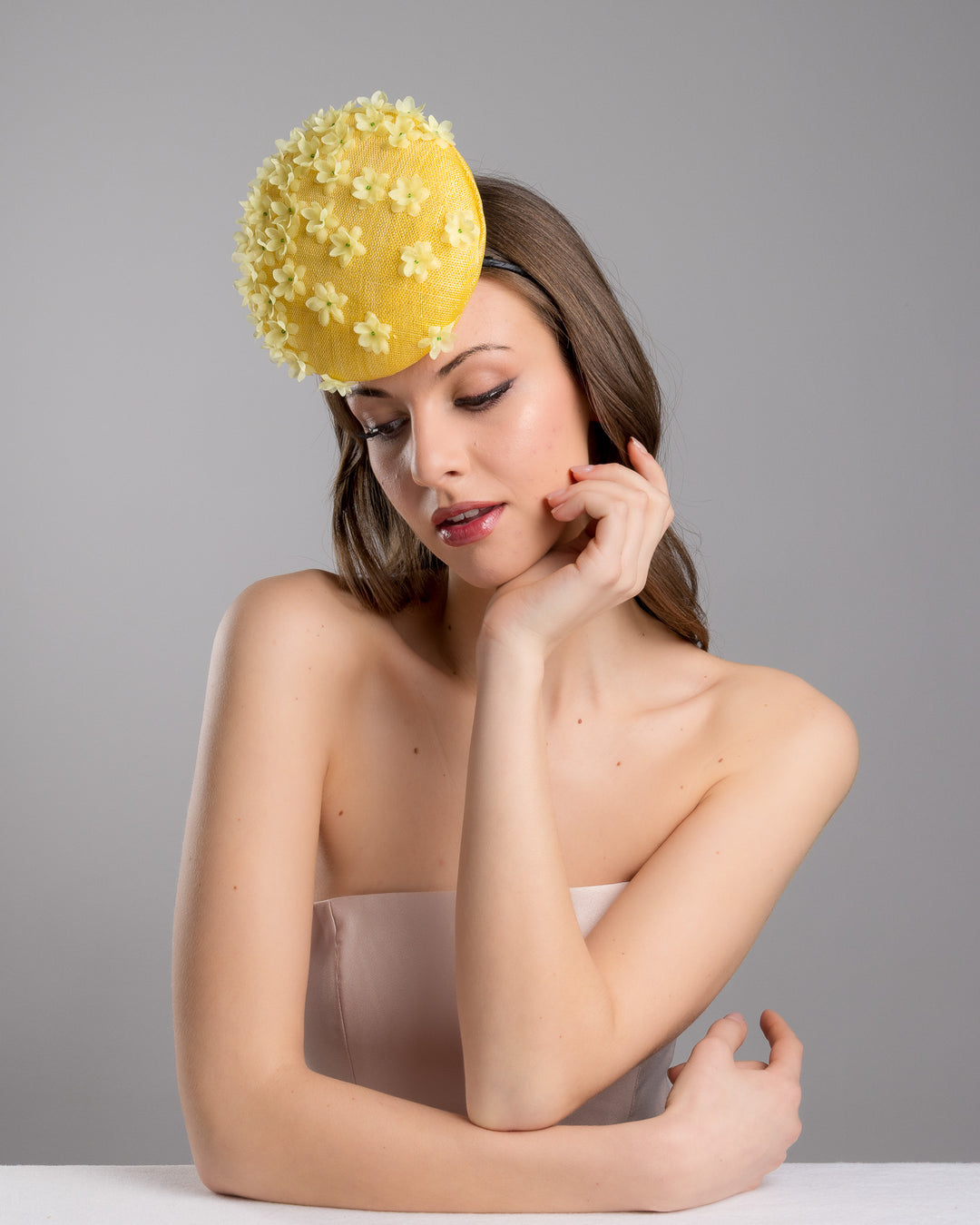 Female model is posing wearing the Dale yellow button shaped fascinator, decorated with yellow organza flowers and green beads. Designed and made by Merve Bayindir Millinery.