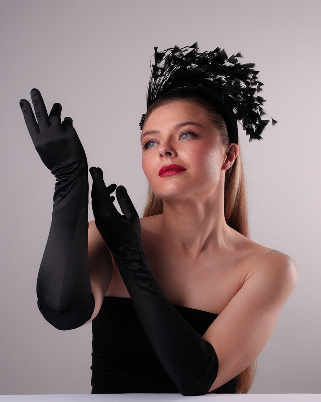 The model is showcasing the front left angle of black velvet high headband decorated with arching layered high goose feathers. Embellished with crystal beads cluster at the edge.