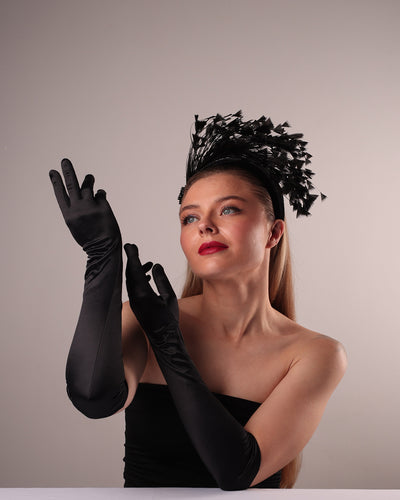 The model is showcasing the front left angle of black velvet high headband decorated with arching layered high goose feathers. Embellished with crystal beads cluster at the edge.