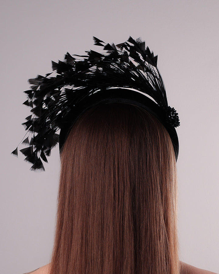 The model is showcasing the back side of black velvet high headband decorated with arching layered high goose feathers. Embellished with crystal beads cluster at the edge.