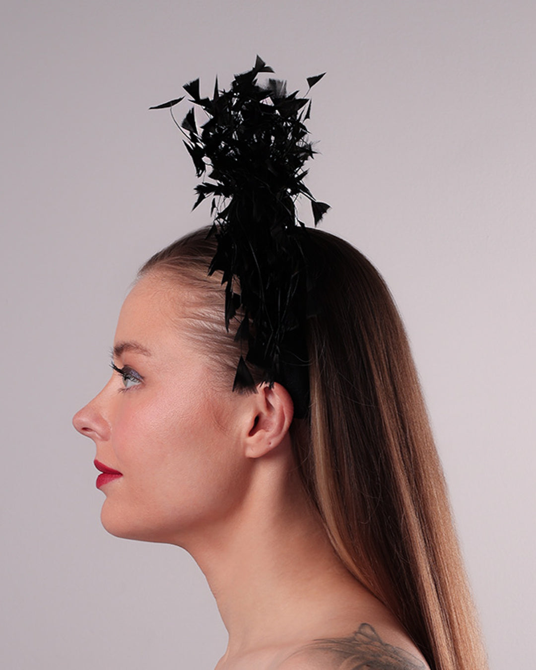 The model is showcasing the left side of black velvet high headband decorated with arching layered high goose feathers. Embellished with crystal beads cluster at the edge.