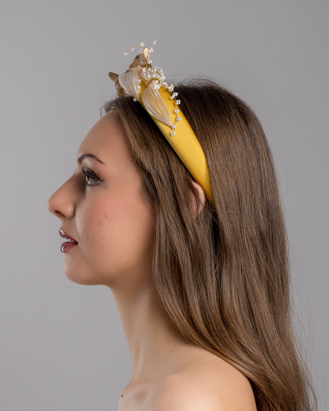 Model is showcasing the left side of the yellow satin headband decorated with bead flowers , resin flowers and leaves with golden wires. Made by Merve Bayindir.