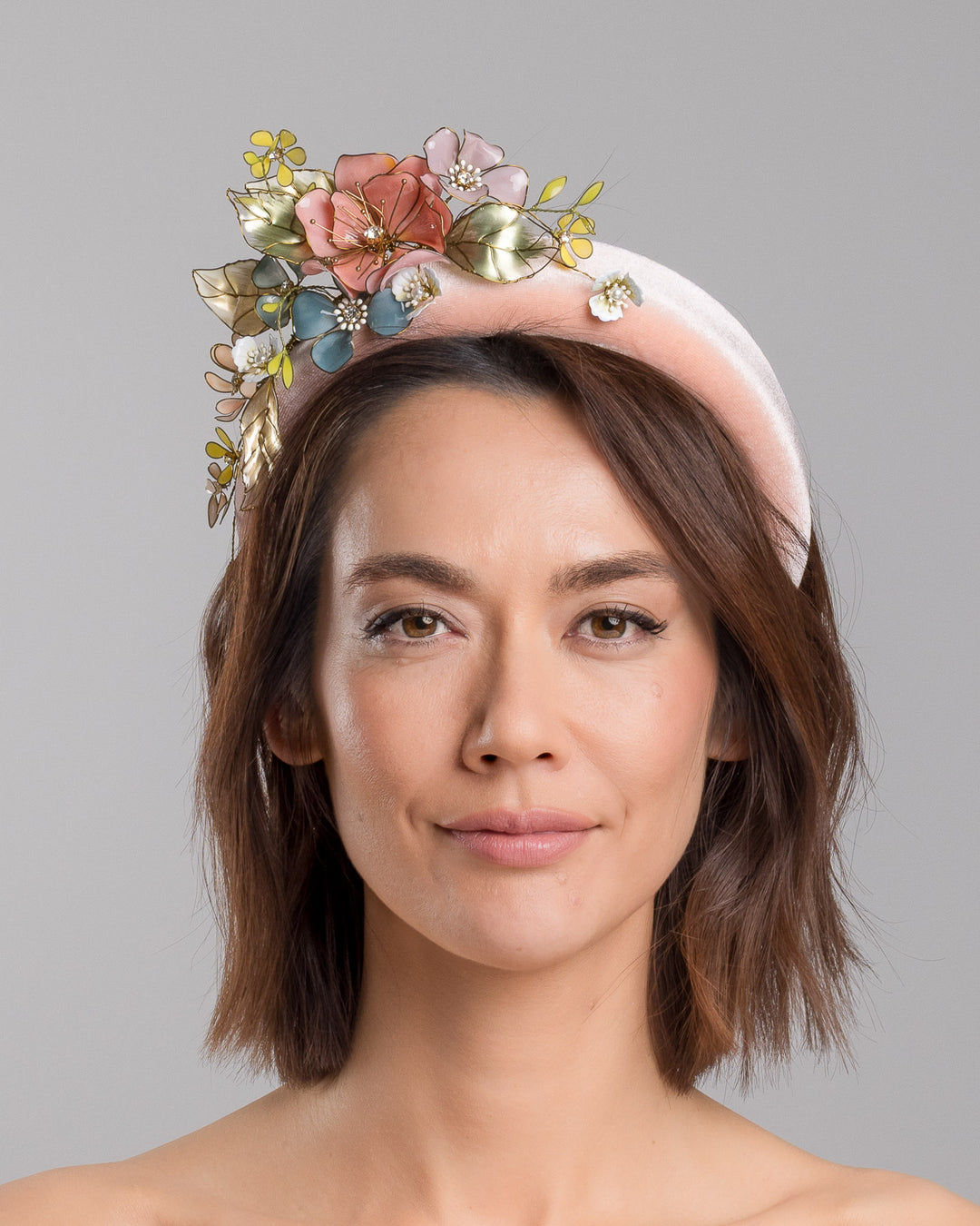 Model is showcasing the front of pink velvet thick headband, decorated with multi coloured resin flower bouquet design. Made by Merve Bayindir millinery.