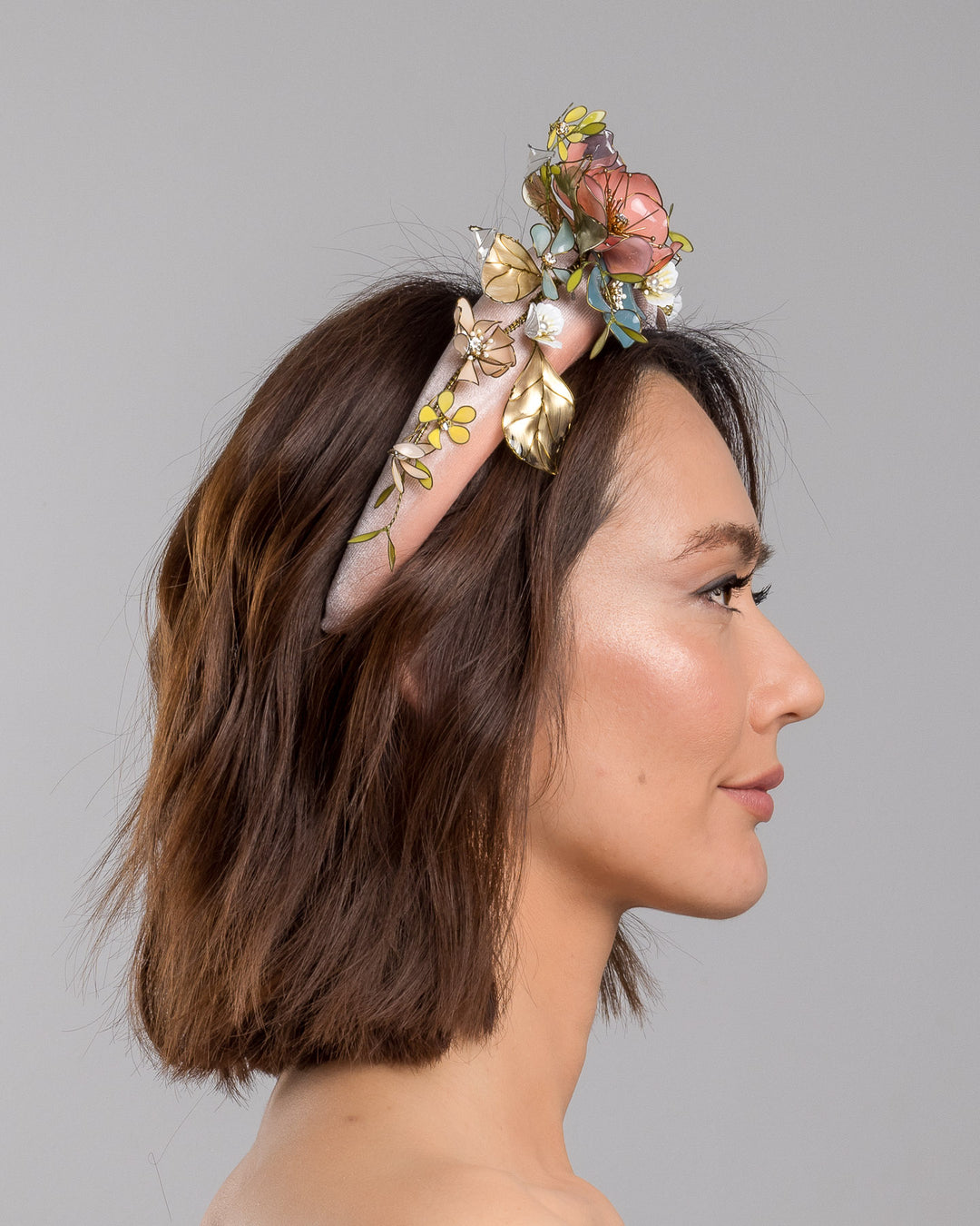 Model is showcasing the right side of pink velvet thick headband, decorated with multi coloured resin flower bouquet design. Made by Merve Bayindir millinery.