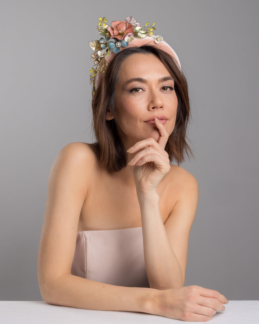 Model is posing wearing Demitto pink velvet thick headband, decorated with multi coloured resin flower bouquet design. Made by Merve Bayindir millinery.
