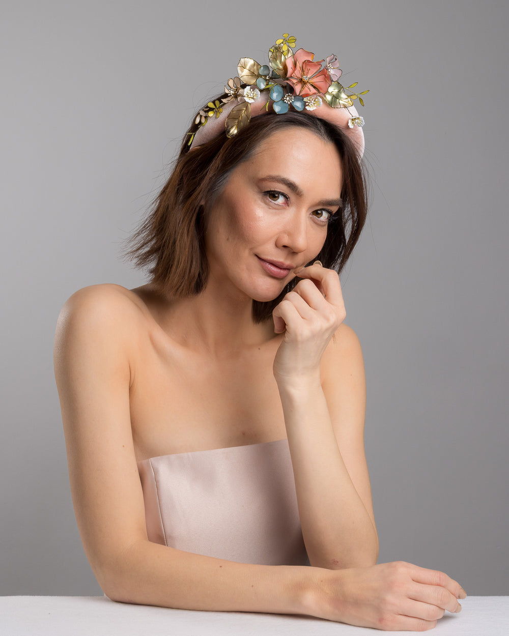 Model is posing wearing Demitto pink velvet thick headband, decorated with multi coloured resin flower bouquet design. Made by Merve Bayindir millinery.
