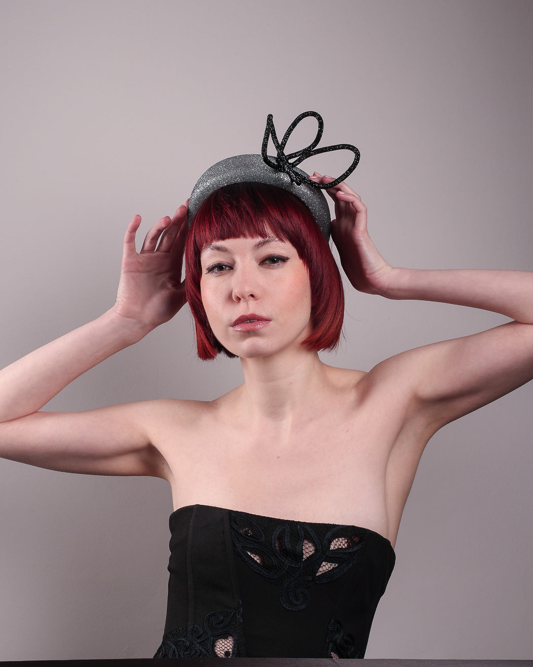 The model showcases the front of the Diamond headband, crafted in shimmering silver with a structured, high headband base. It features a sculptural, black rhinestone-embellished abstract flower that arcs confidently upward. Designed by Merve Bayindir.