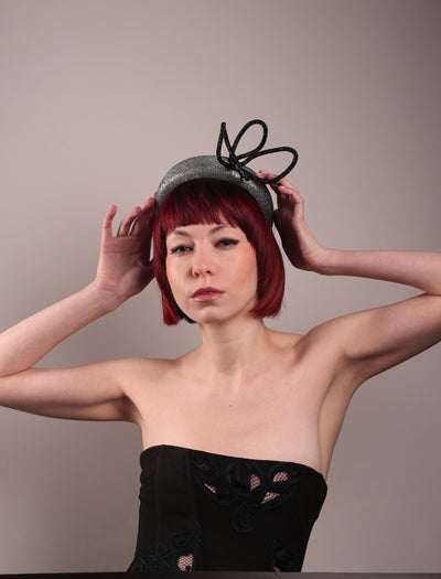 The model showcases the front of the Diamond headband, crafted in shimmering silver with a structured, high headband base. It features a sculptural, black rhinestone-embellished abstract flower that arcs confidently upward. Designed by Merve Bayindir.