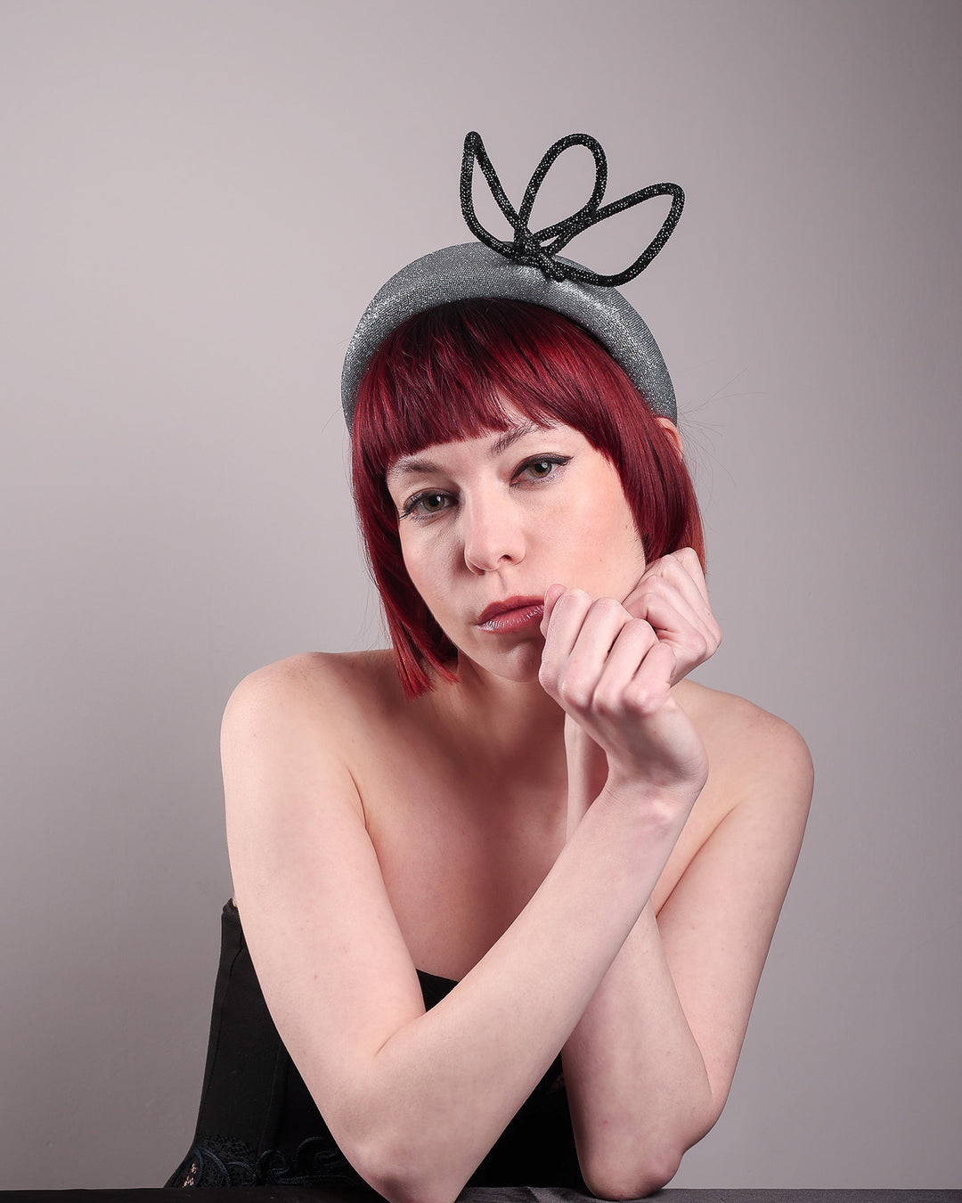 The model showcases the right front of the Diamond headband, crafted in shimmering silver with a structured, high headband base. It features a sculptural, black rhinestone-embellished abstract flower that arcs confidently upward. Designed by Merve Bayindir.