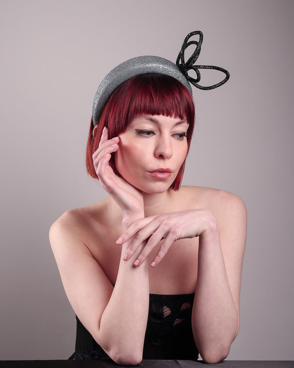 The model showcases the left front side of the Diamond headband, crafted in shimmering silver with a structured, high headband base. It features a sculptural, black rhinestone-embellished abstract flower that arcs confidently upward. Designed by Merve Bayindir.