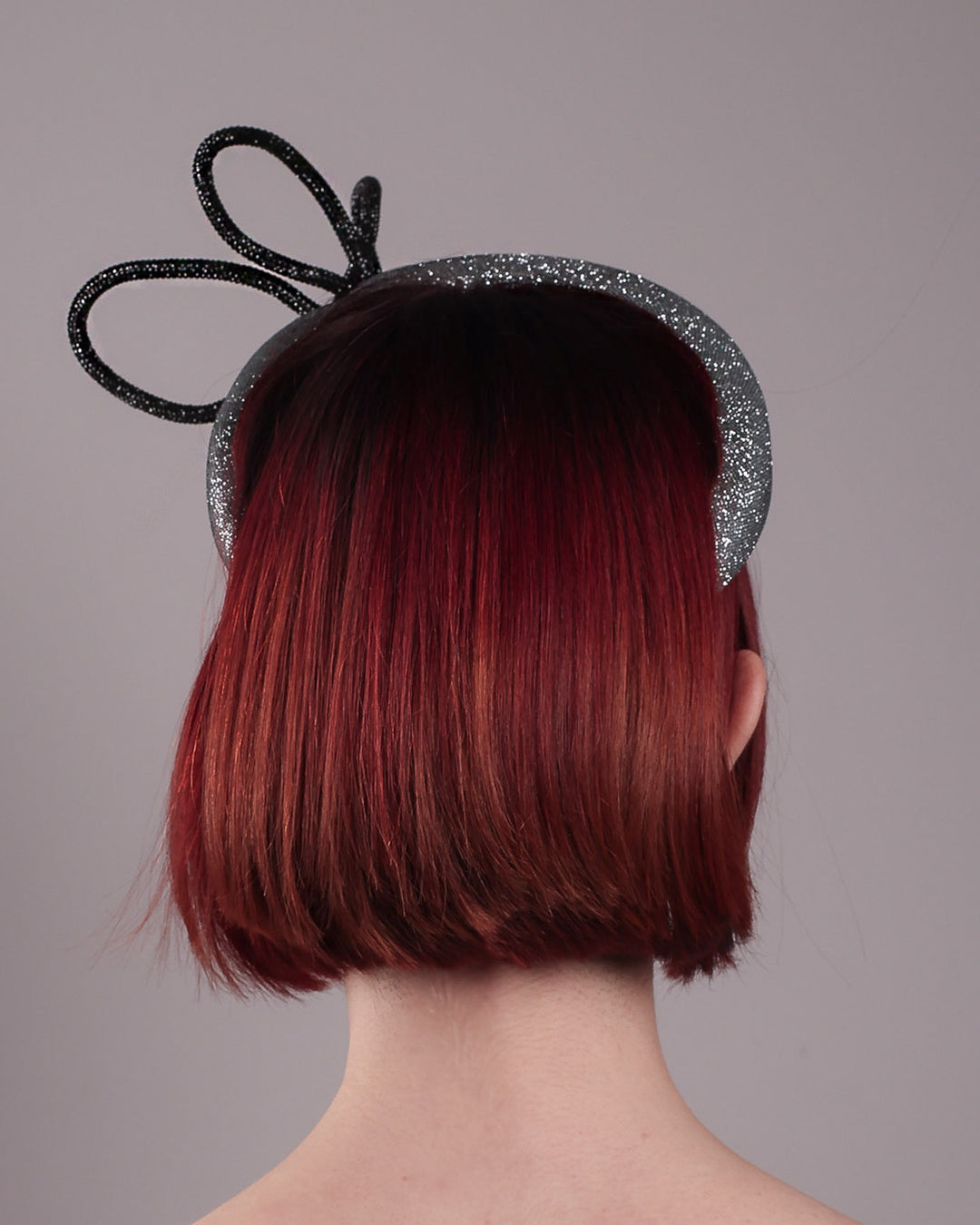 The model showcases the back of the Diamond headband, crafted in shimmering silver with a structured, high headband base. It features a sculptural, black rhinestone-embellished abstract flower that arcs confidently upward. Designed by Merve Bayindir.