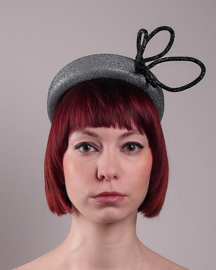 The model showcases the front close up of the Diamond headband, crafted in shimmering silver with a structured, high headband base. It features a sculptural, black rhinestone-embellished abstract flower that arcs confidently upward. Designed by Merve Bayindir.