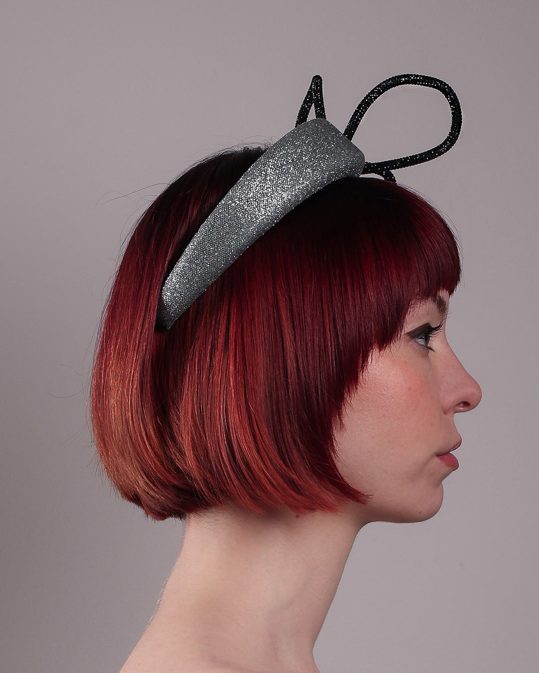 The model showcases the right side close up of the Diamond headband, crafted in shimmering silver with a structured, high headband base. It features a sculptural, black rhinestone-embellished abstract flower that arcs confidently upward. Designed by Merve Bayindir.