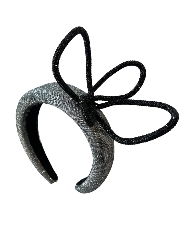 Still life picture of the front of the Diamond headband, crafted in shimmering silver with a structured, high headband base. It features a sculptural, black rhinestone-embellished abstract flower that arcs confidently upward. Designed by Merve Bayindir.