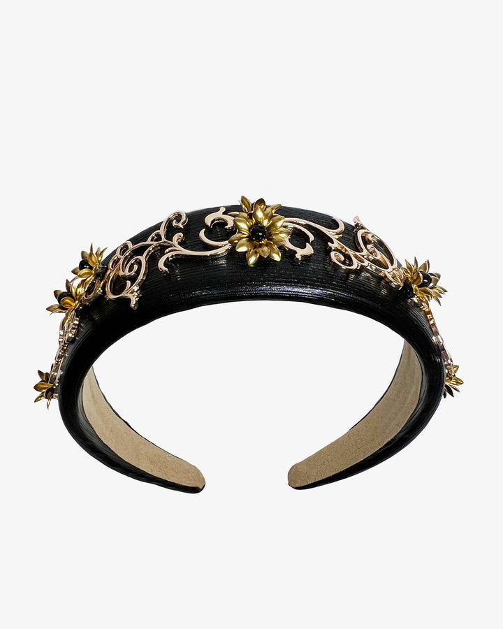 Wide black satin headband embellished with ornate gold filigree scrollwork and small metallic floral accents, creating a regal, baroque-inspired statement design.
Designed and made by Merve Bayindir Millinery.
