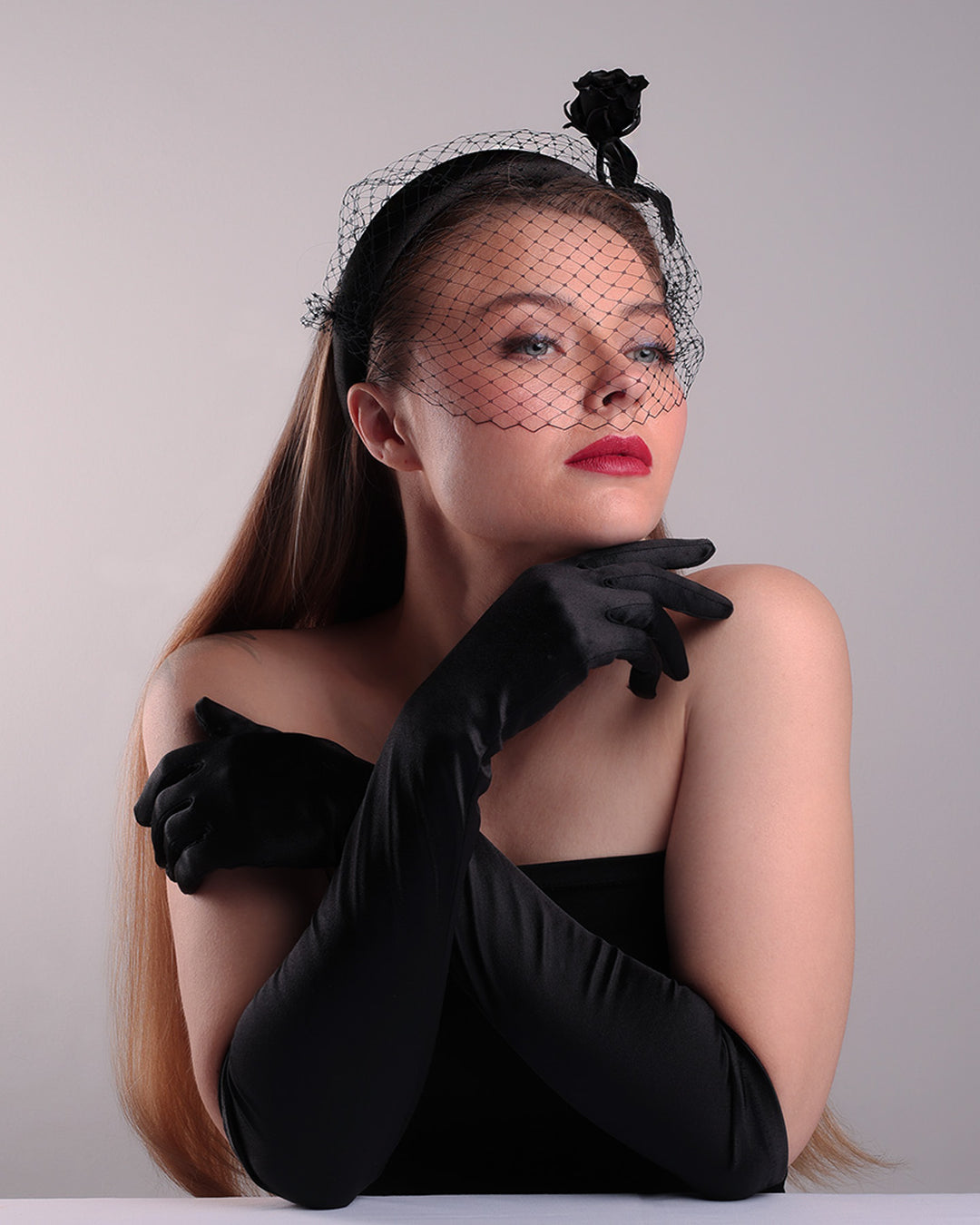 Model is showcasing the right  below angle side of semi high black silk heaband with a black veil adroned with a handmade black sateen rose on the right side.