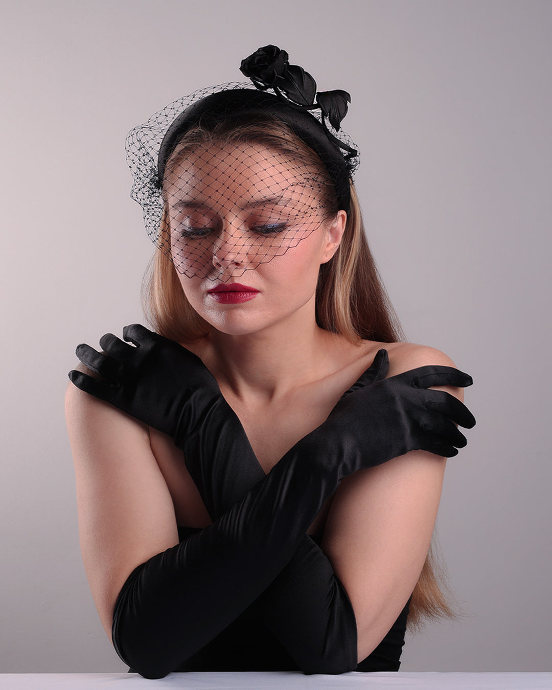Model is showcasing the front left side of semi high black silk heaband with a black veil adroned with a handmade black sateen rose on the right side.