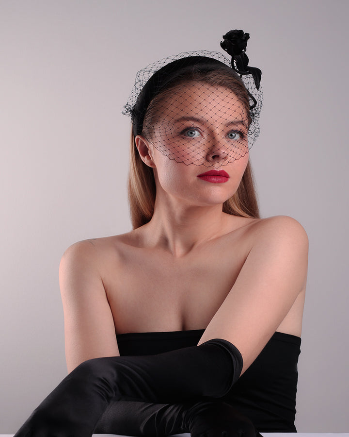 Model is showcasing the front right side of semi high black silk heaband with a black veil adroned with a handmade black sateen rose on the right side.