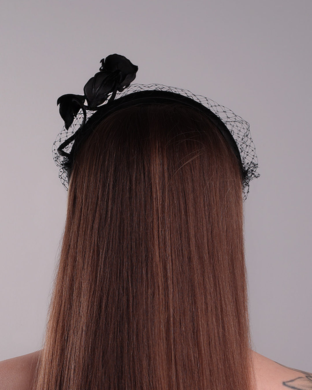 Model is showcasing the back side of semi high black silk heaband with a black veil adroned with a handmade black sateen rose on the right side.