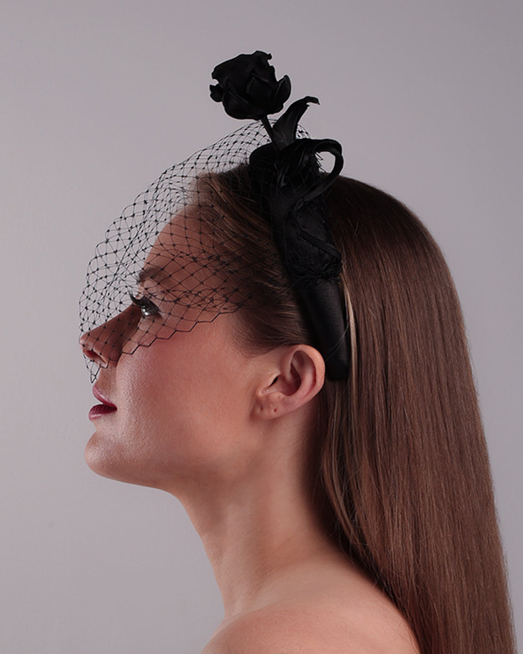 Model is showcasing the left side of semi high black silk heaband with a black veil adroned with a handmade black sateen rose on the right side.