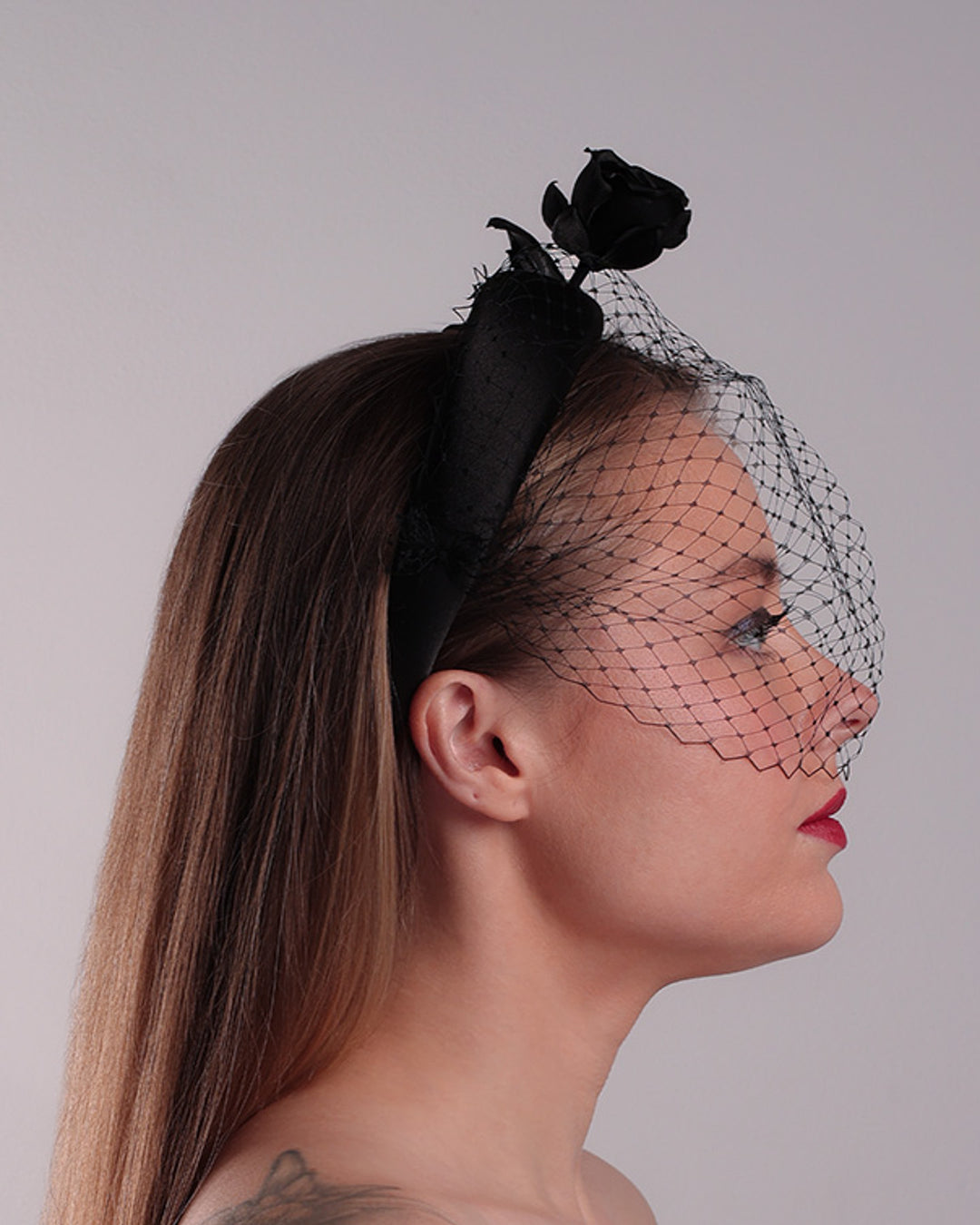 Model is showcasing the right side of semi high black silk heaband with a black veil adroned with a handmade black sateen rose on the right side.