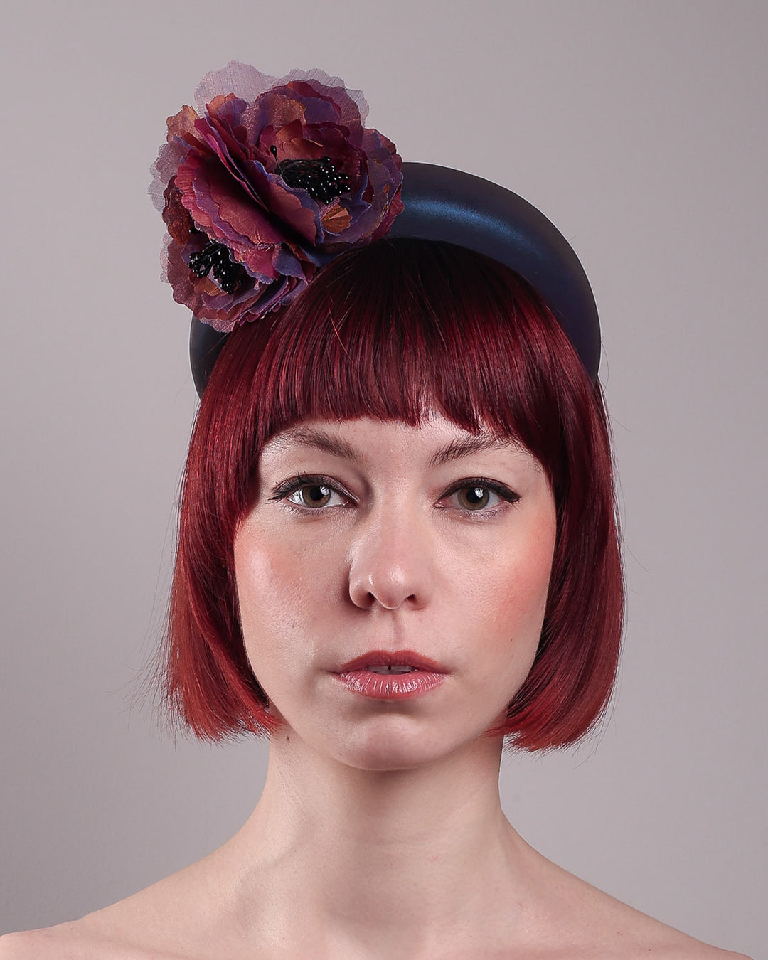 Model wearing and showcasing the straight front close up of an iridescent Eclipse Headband with layered flower detail in deep purple, bronze, and wine tones, handcrafted by Merve Bayindir.