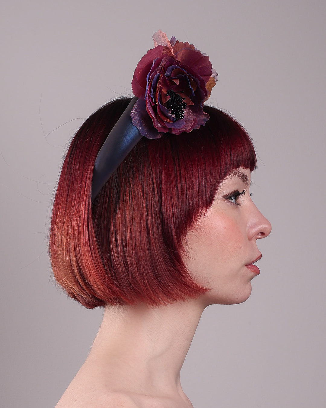 Model wearing and showcasing the left side close up of an iridescent Eclipse Headband with layered flower detail in deep purple, bronze, and wine tones, handcrafted by Merve Bayindir.