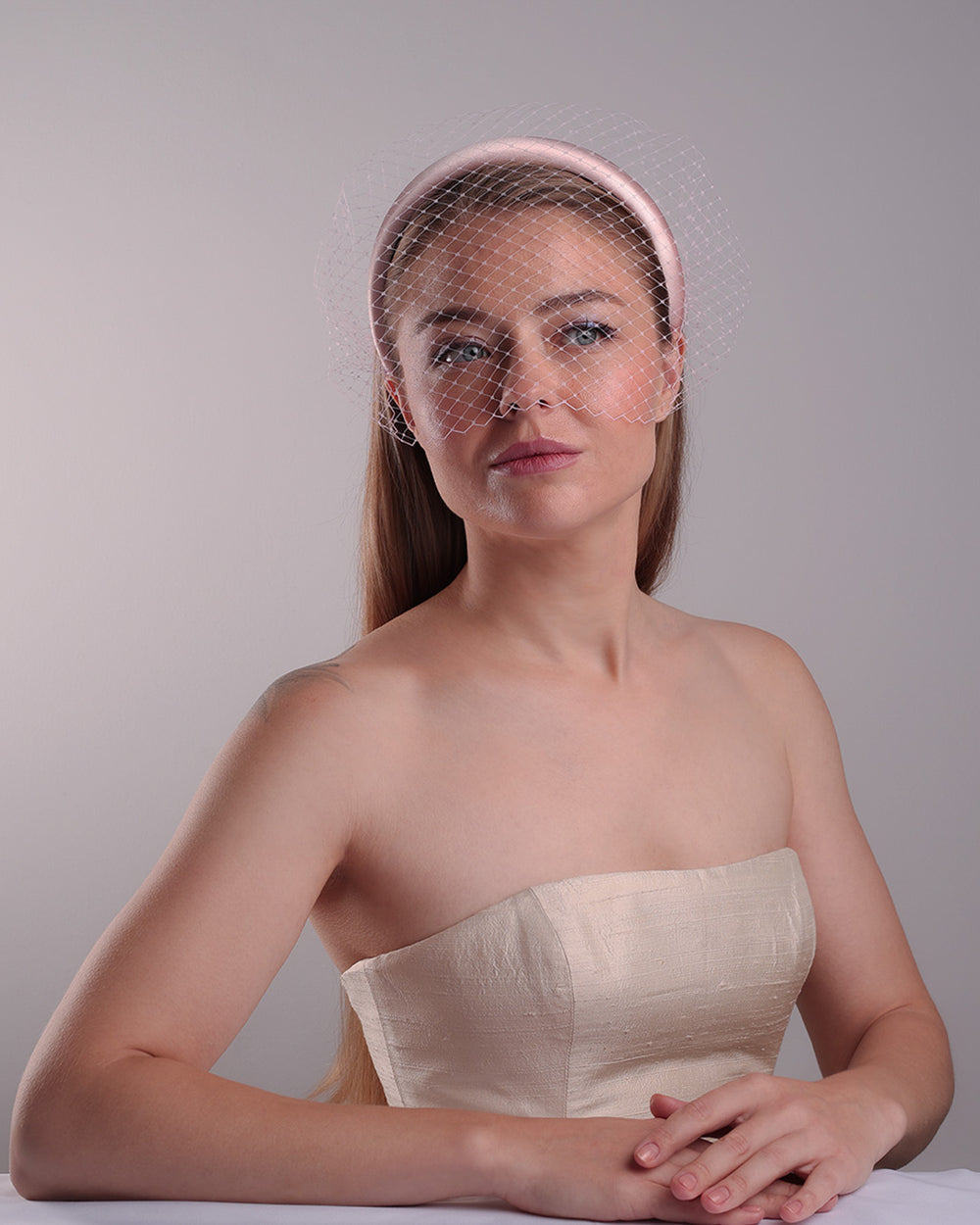 Model is presenting the fornt of a thin slightly high, silk pink headband that is embellished with a pink veil.