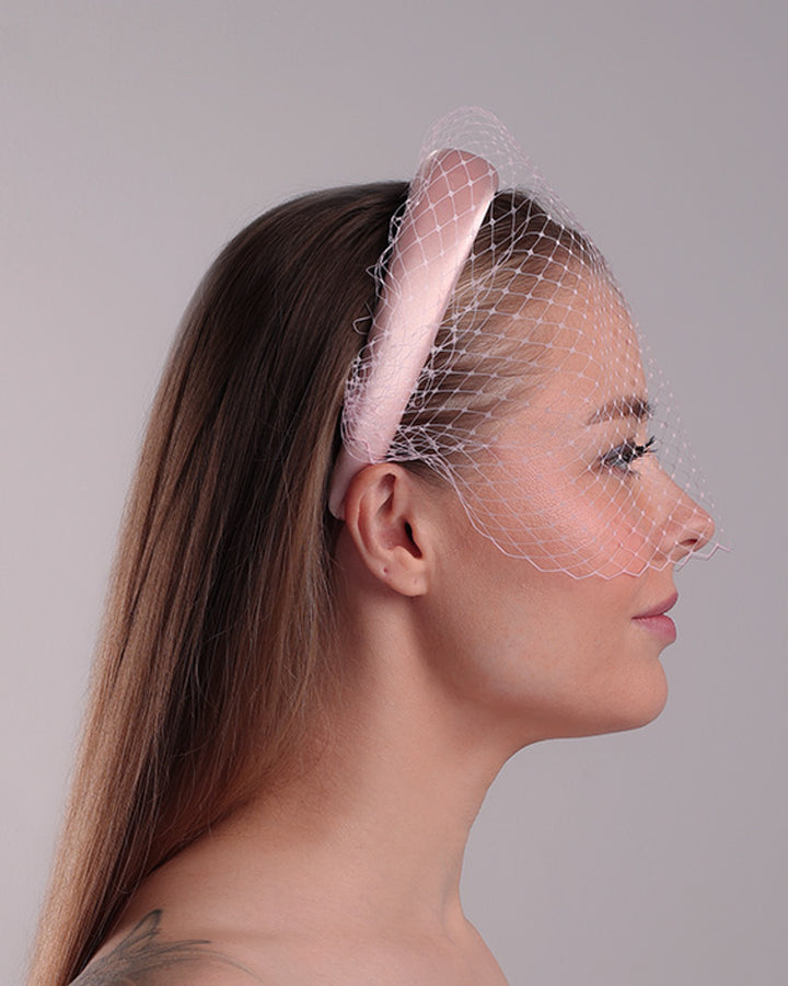Model is presenting the right side of a thin slightly high, silk pink headband that is embellished with a pink veil.