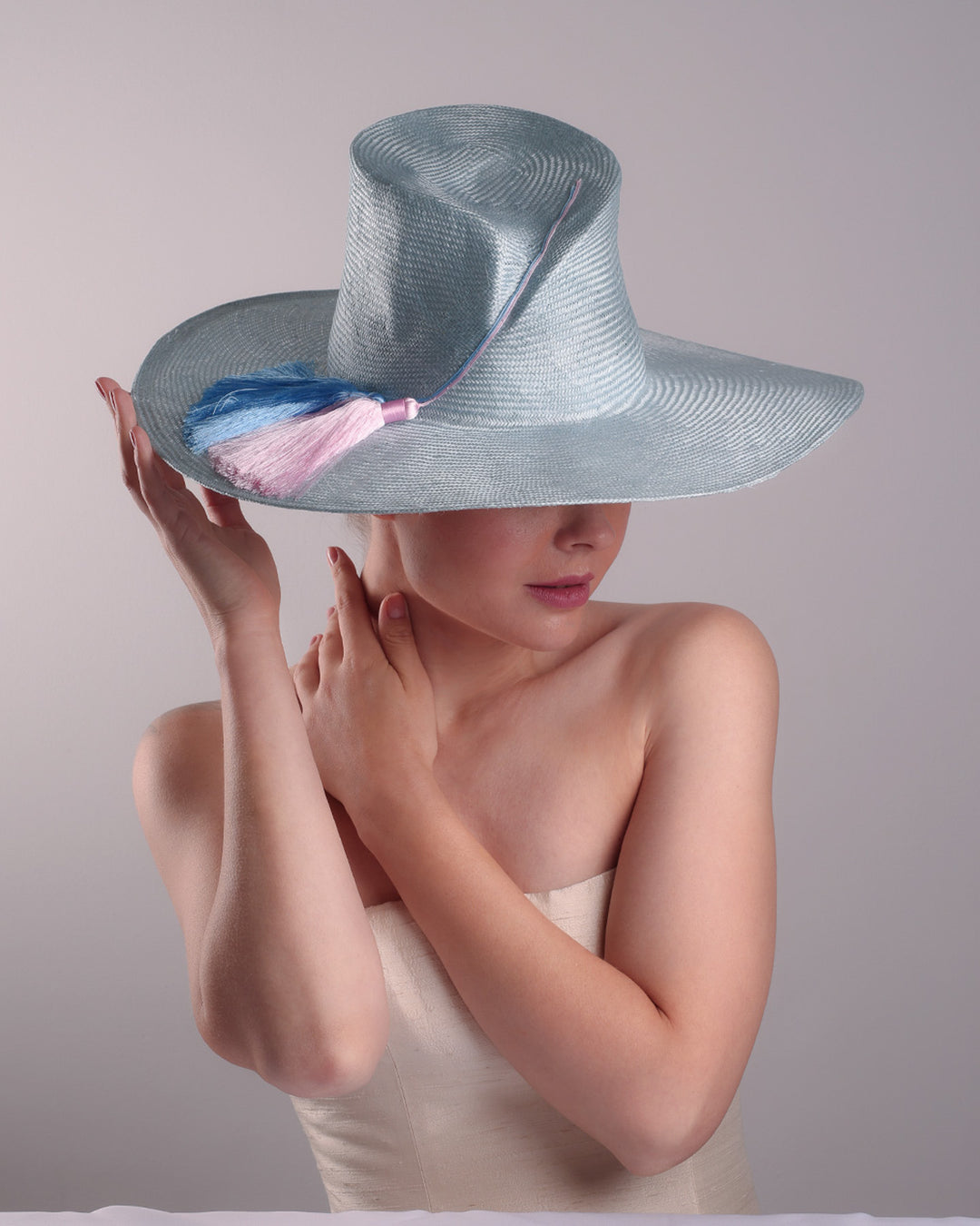 Model is presenting the top front blue parasisal hat with asymetric crown and wide brim. Decorated with blue and pink tassels.