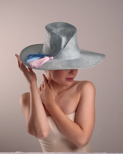 Model is presenting the top front blue parasisal hat with asymetric crown and wide brim. Decorated with blue and pink tassels.