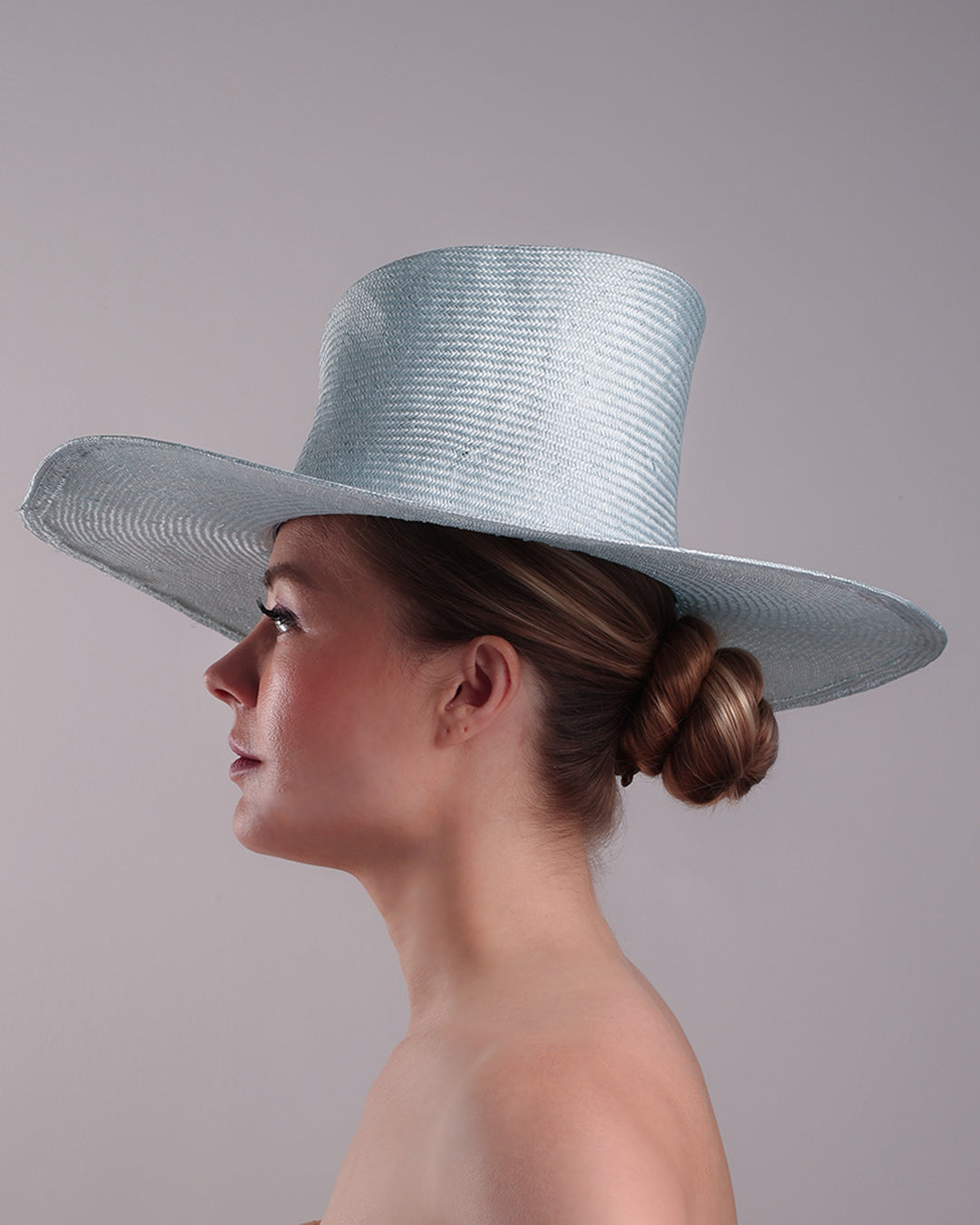 Model is presenting the left side of a blue parasisal hat with asymetric crown and wide brim. Decorated with blue and pink tassels.