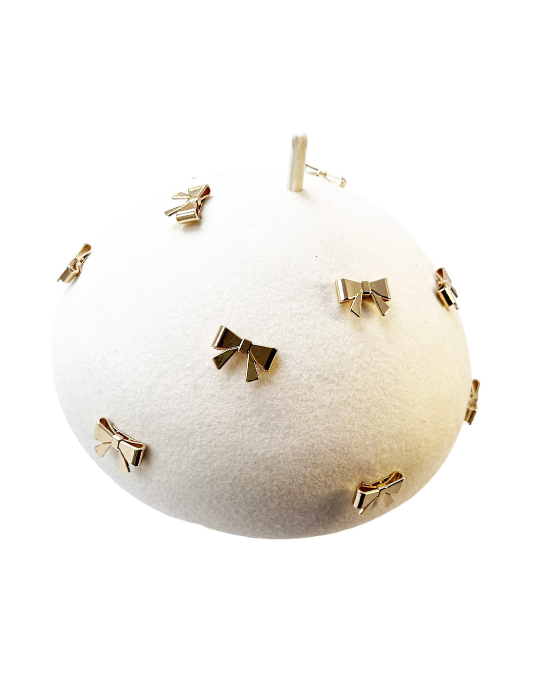 Still life picture of the dome-shaped, round Elodie pillbox beret hat, crafted from soft white felt and adorned with gold coloured metal bows. Designed by Merve Bayindir.