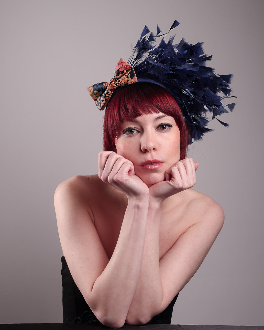 The model showcases the front of Esmee, where a navy storm of fine-cut feathers bursts from the same-coloured Alice headband, like smoke in reverse, anchored by a flower motif printed on a textured crock wood bow. Designed by Merve Bayindir.