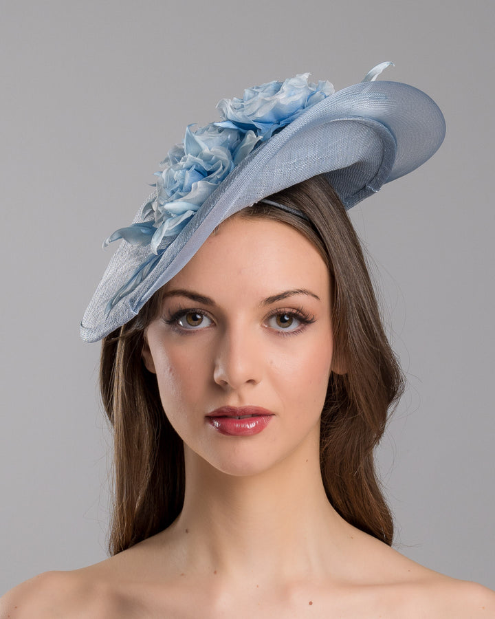 The model is showcasing the front  side close up of the powder blue sinamay fascinator with a sculpted teardrop silhouette, adorned with layered chiffon roses and matching soft leaves for an elegant, romantic finish. Designed and made by Merve Bayindir Millinery.
