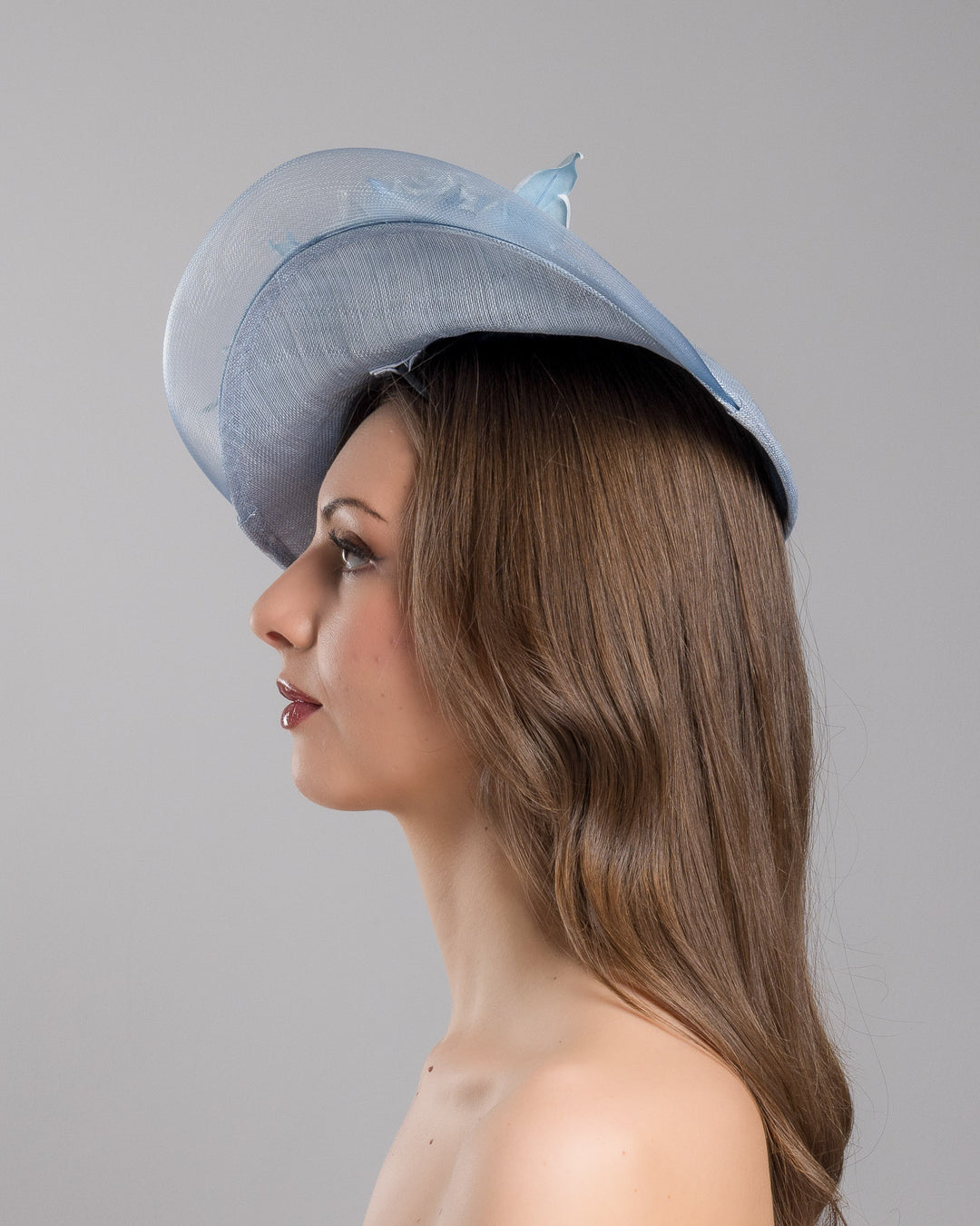The model is showcasing the left side close up of the powder blue sinamay fascinator with a sculpted teardrop silhouette, adorned with layered chiffon roses and matching soft leaves for an elegant, romantic finish. Designed and made by Merve Bayindir Millinery.
