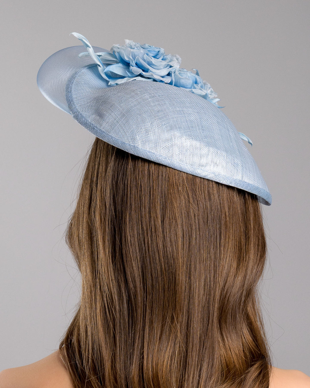 The model is showcasing the back side close up of the powder blue sinamay fascinator with a sculpted teardrop silhouette, adorned with layered chiffon roses and matching soft leaves for an elegant, romantic finish. Designed and made by Merve Bayindir Millinery.
