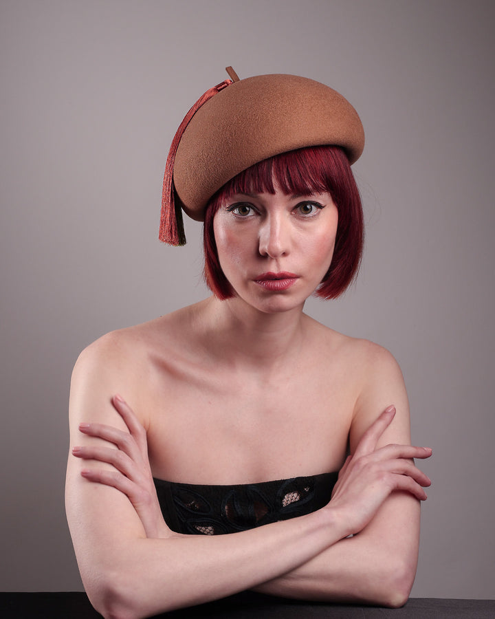 The model is showcasing the front view of the Faye Beret Hat, handcrafted in camel wool felt. It&