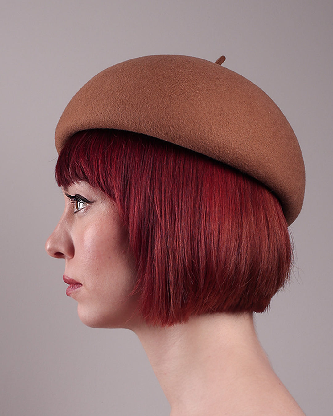 The model is showcasing the left side close up of the Faye Beret Hat, handcrafted in camel wool felt. It&