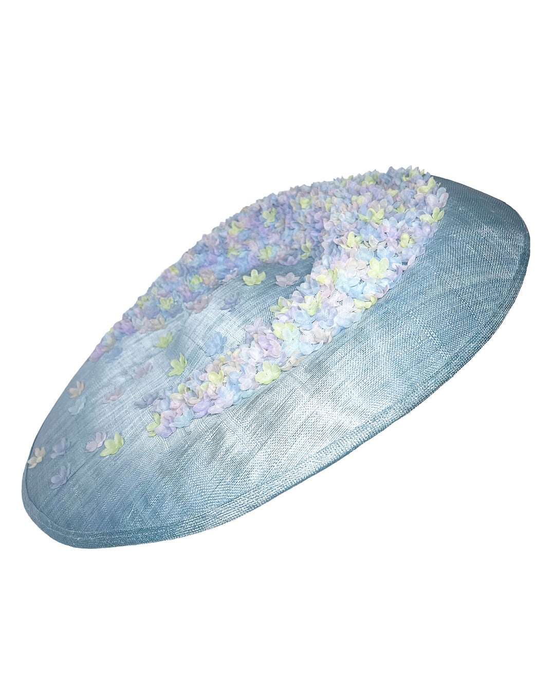 Powder blue sinamay base hat with a wide, gently sloping brim, adorned with clusters of soft pastel organza flowers in lilac, pale yellow, and blush tones that gather along the crown and trail lightly across the surface. Designed and made by Merve Bayindir Millinery.

