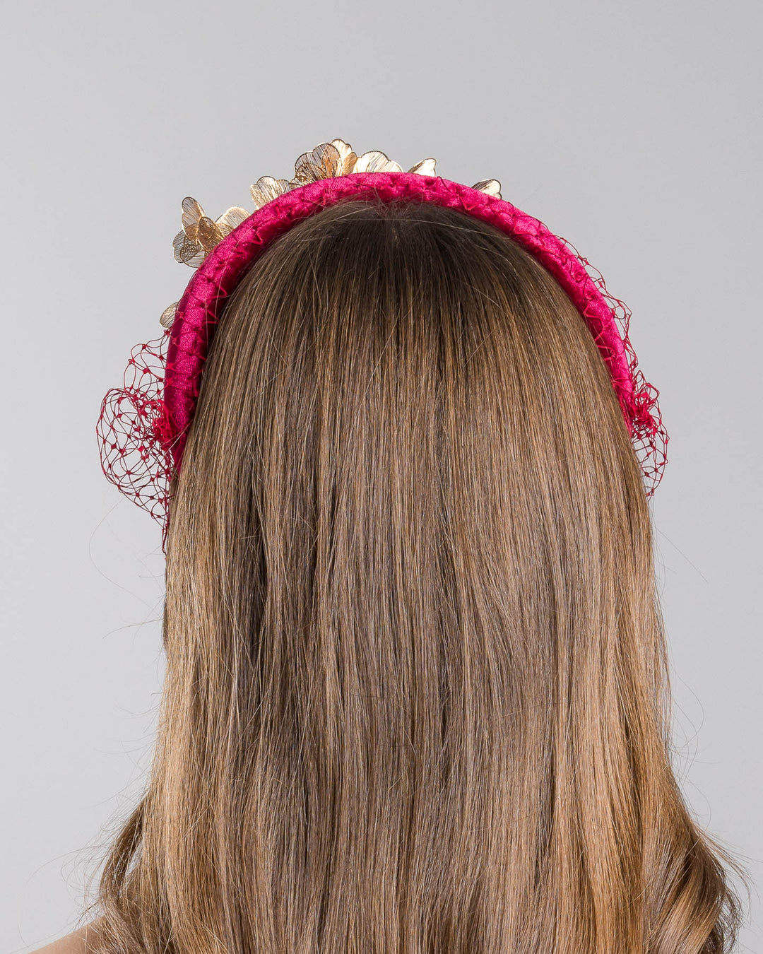 Model is showcasing the back of the wine coloured velvet headband declared with laser cut gold coloured wire flowers and finished with a red veil. Made by Merve bayindir millinery.