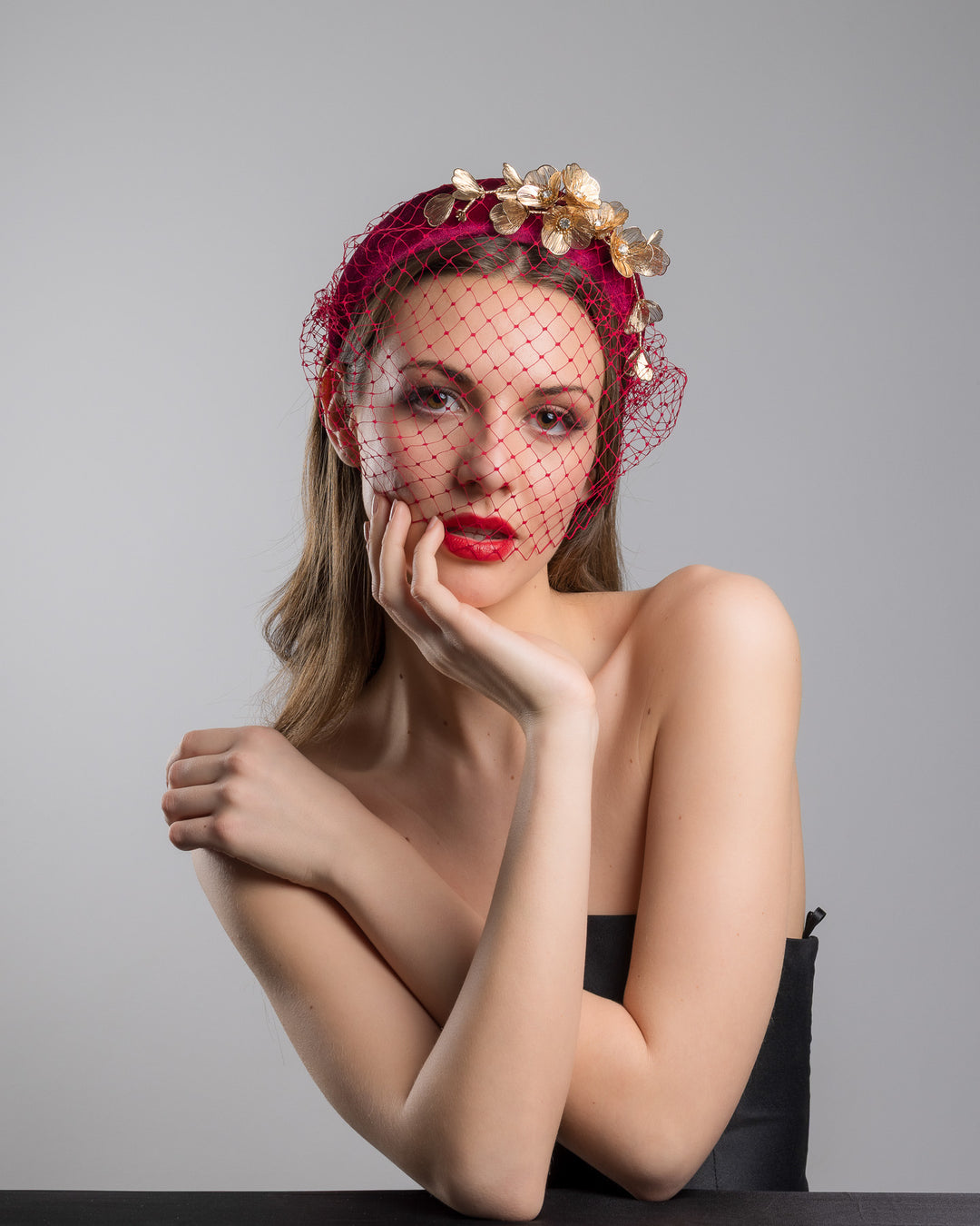 Model is posing wearing the wine coloured Fiducia velvet headband declared with laser cut gold coloured wire flowers and finished with a red veil. Made by Merve bayindir millinery.